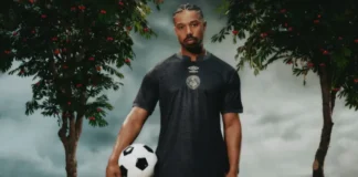 Michael B Jordan wearing black AFC Bournemouth kit holding soccer ball with cherry trees