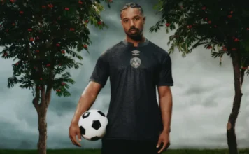 Michael B Jordan wearing black AFC Bournemouth kit holding soccer ball with cherry trees