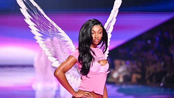 Angel Reece in Angel Wings - Victoria Secret Fashion Show Performance Angel Reece wearing white feathered angel wings and pink embellished outfit on purple-lit runway